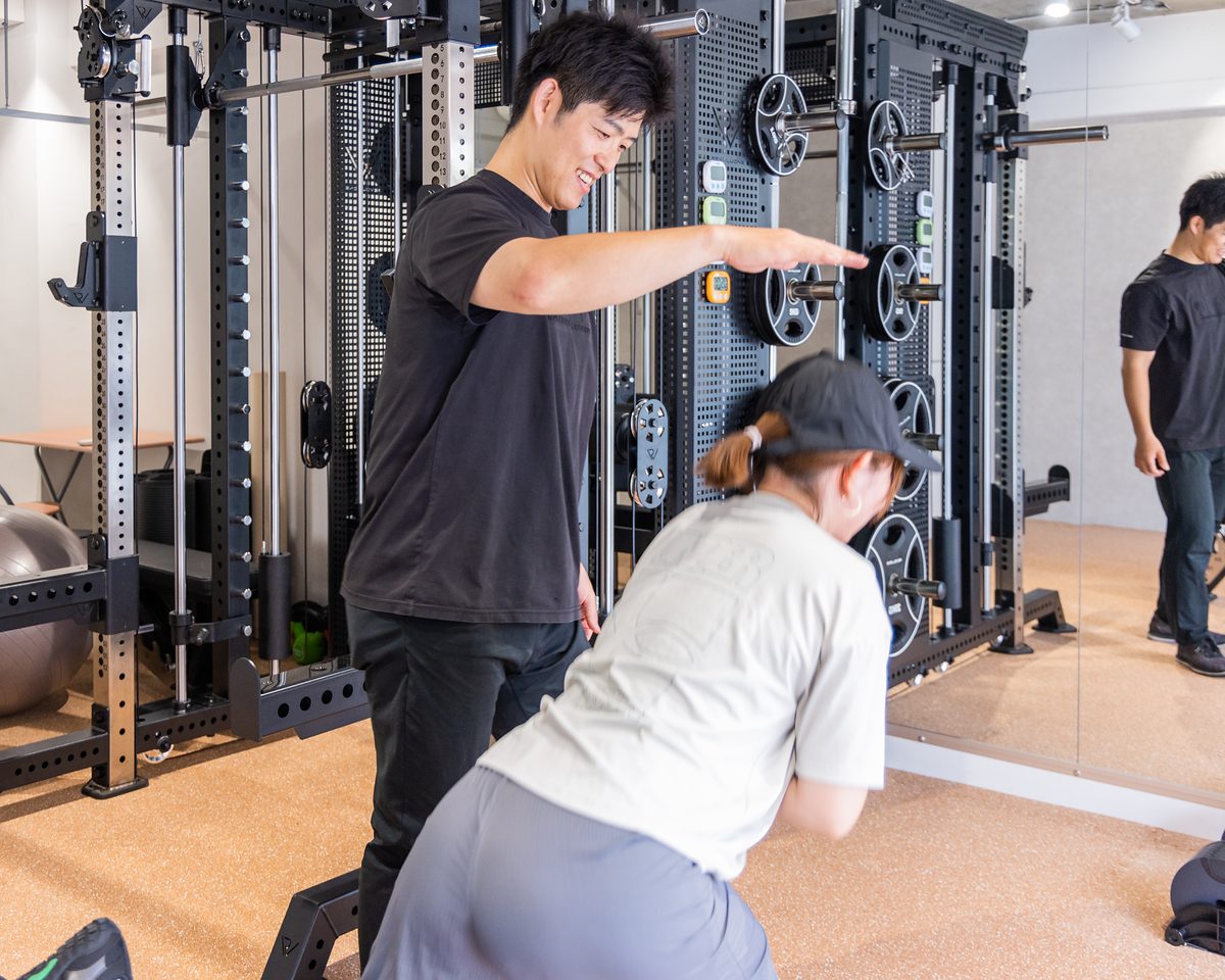 ラックの前で、トレーナーが腕の角度を示しながら会員の動きを確認している様子