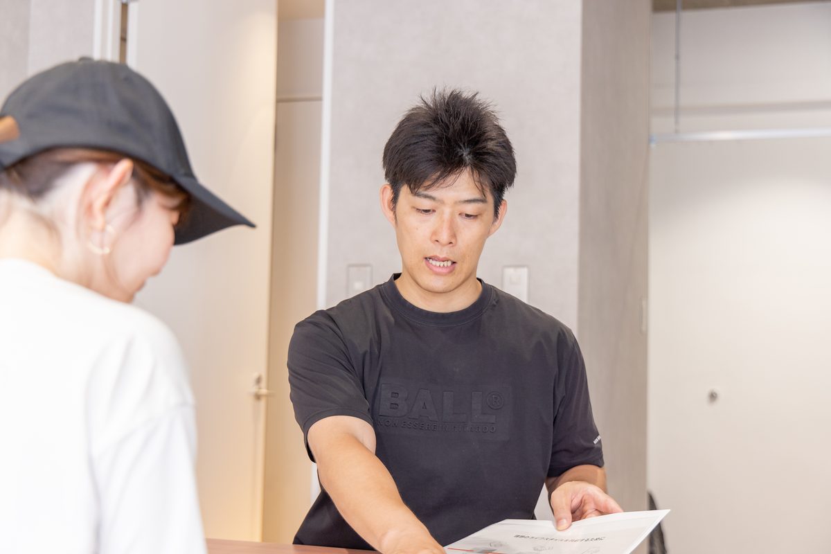カウンター越しに資料を示しながら話すトレーナーと、向かい合って聞く来店者