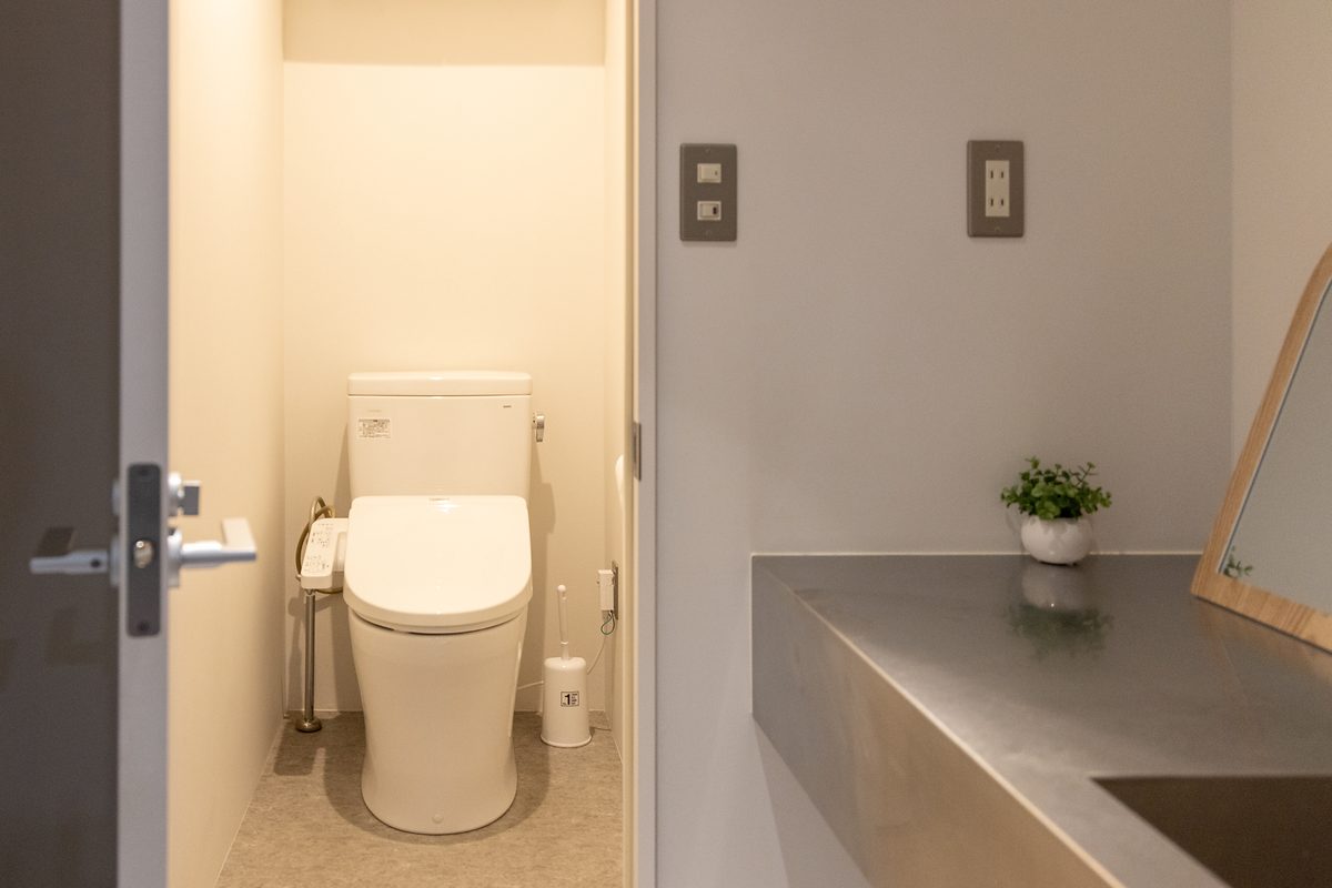 扉の奥に見える手洗い付きのトイレと、隣り合う洗面カウンター