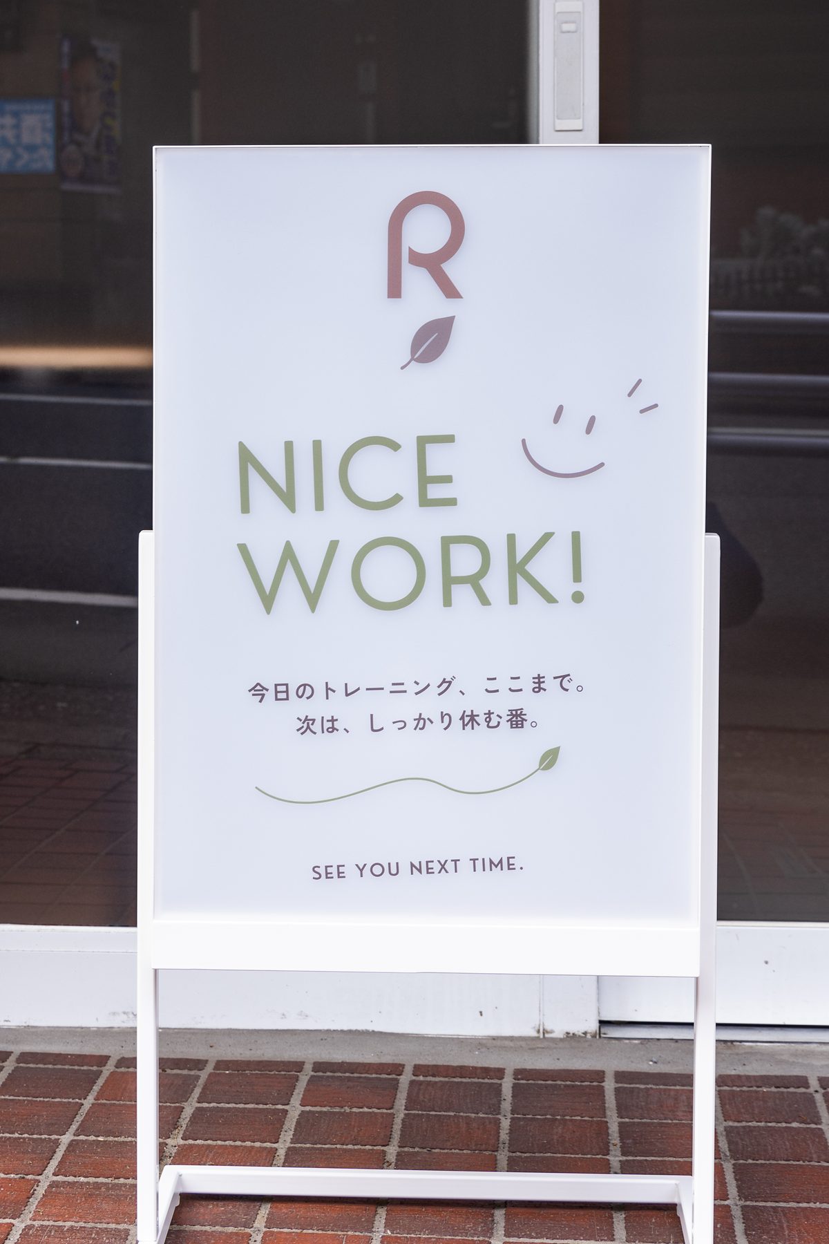 店頭の立て看板。「NICE WORK! 今日のトレーニング、ここまで。次は、しっかり休む番。」の言葉